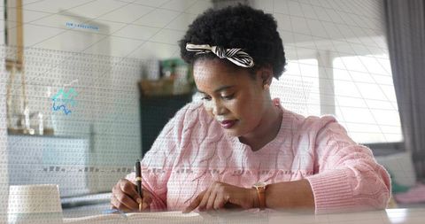 Writing at home desk in pink sweater focusing on notebook, pen and productivity
