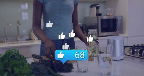 Woman preparing green smoothie on modern kitchen island while receiving social media likes