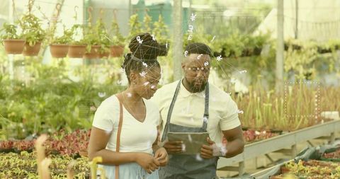 Greenhouse staff advising customer with tablet while inspecting nursery plants