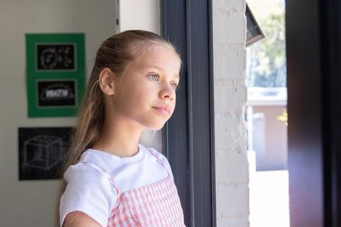 Preteen girl looking out window, daylight contemplative portrait in home interior