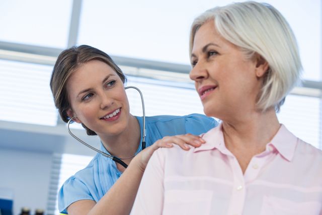 Doctor examining senior patient with stethoscope in clinic. Ideal for healthcare, medical services, senior care, and health insurance promotions. Useful for illustrating doctor-patient interactions, medical checkups, and professional healthcare environments.