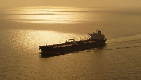 Crude oil tanker gliding across golden sea at sunset with dramatic silhouette and wake