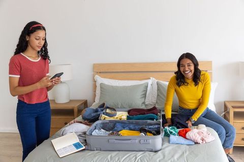 Diverse mother and teenage daughter packing suitcase on bed preparing for family trip