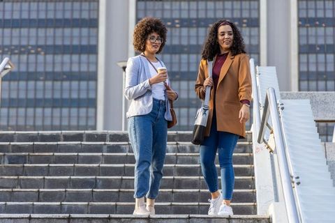 Two professional women walking down urban stairs holding coffee and bags