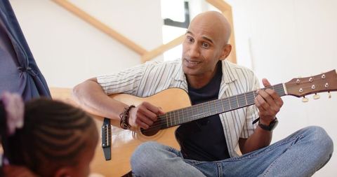 Father teaching guitar to daughter at home, acoustic guitar lesson, family bonding