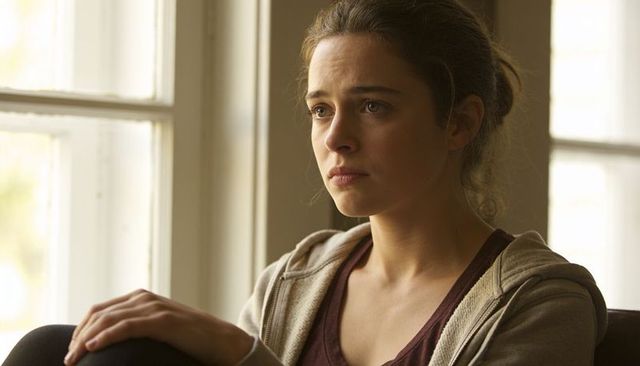 Young woman sitting by window looking contemplative and pensive in natural daylight