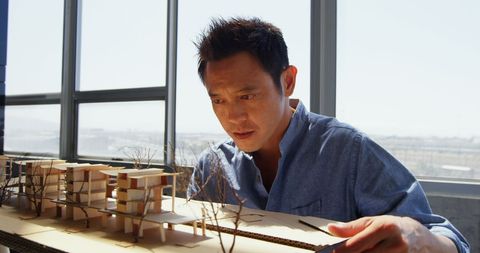 Focused Asian Architect Examining Scale Model in Modern Office