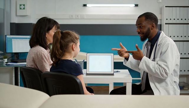 Male doctor pointing and explaining treatment to child and parent during clinic consultation