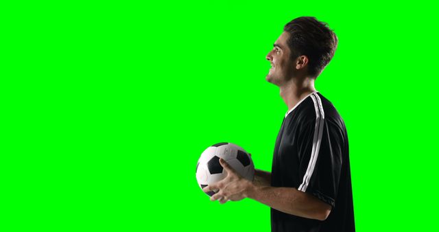 Male soccer player in uniform holding soccer ball, standing sideways against green screen background. Suitable for sports promotions, advertisements, training videos, or digital edits with custom backgrounds.