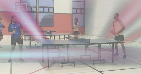 Coed athletes playing table tennis in indoor gym wearing sportswear with lens flare