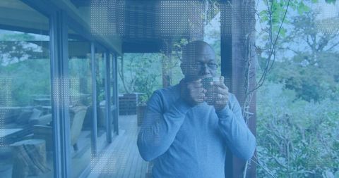 Mature man sipping coffee on wooden porch, relaxing with ceramic mug and garden view