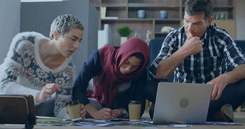 Multicultural team collaborating on floor with laptop and papers, brainstorming ideas