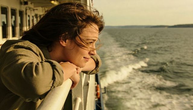 Windswept woman leaning on ferry rail gazing at sunlit ocean horizon during coastal travel