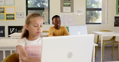Elementary students learning on laptops in bright classroom with geometry posters