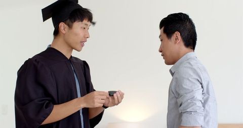 Father congratulating son graduation gown achievement