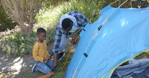African american father and son assembling blue tent in backyard garden camping bonding