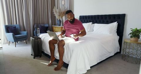 Man Booking Travel Online with Laptop in Cozy Bedroom