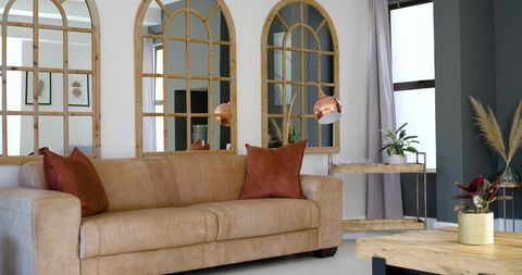 Tan leather loveseat with rust pillows and arched mirrors in contemporary living room