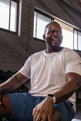 Smiling fit african man resting on gym bench wearing smartwatch and athletic wear
