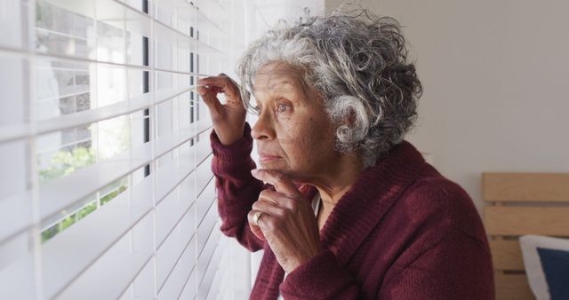Thoughtful senior african american woman looking through window. Retirement and spending time at home concept.