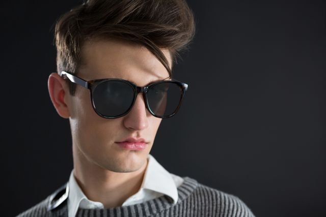 This image features an androgynous man wearing sunglasses, posing confidently against a black background. Ideal for use in fashion editorials, eyewear advertisements, style blogs, and modern lifestyle promotions.