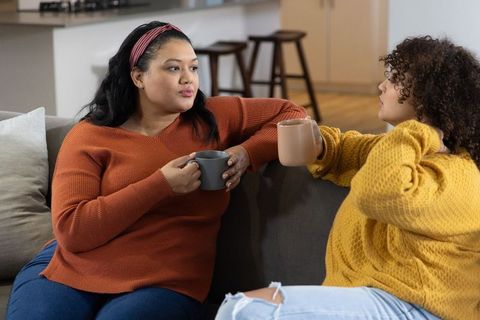 Cozy living room chat between diverse women holding mugs in knit sweaters