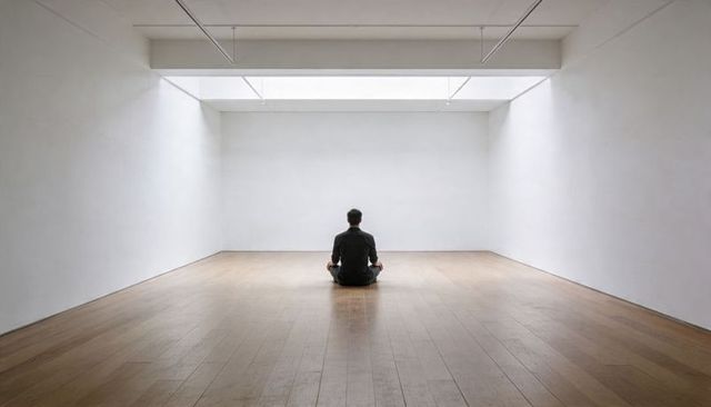 Solitary man meditating in minimalist white gallery under skylight on wooden floor