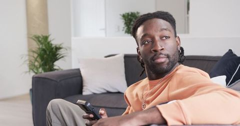 African American man relaxing on sofa holding TV remote in contemporary living room