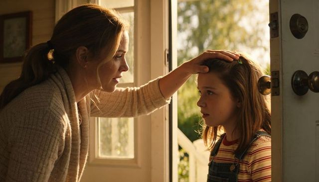 Mother checking daughter's forehead at sunlit doorway showing care and comfort