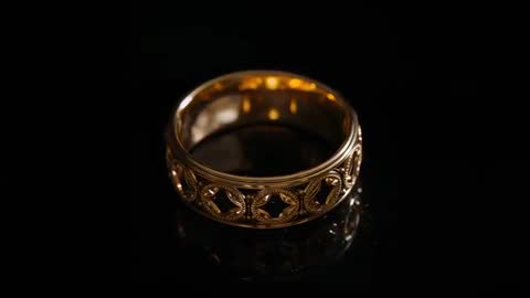 Rotating ornate gold filigree ring catching reflections and sparkling glints on black surface