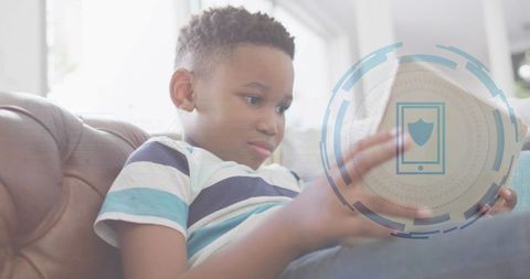 Boy tapping tablet on sofa showing digital security shield overlay for safe learning