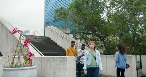 Multicultural pedestrians walking down concrete plaza stairs near pink flowering planter