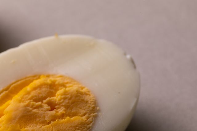 This image shows a close-up of a halved boiled egg on a white background. The focus is on the egg yolk and egg white, highlighting the texture and color contrast. Ideal for use in articles or advertisements related to healthy eating, nutrition, protein-rich diets, breakfast ideas, and simple food presentations. The copy space allows for easy addition of text or branding.