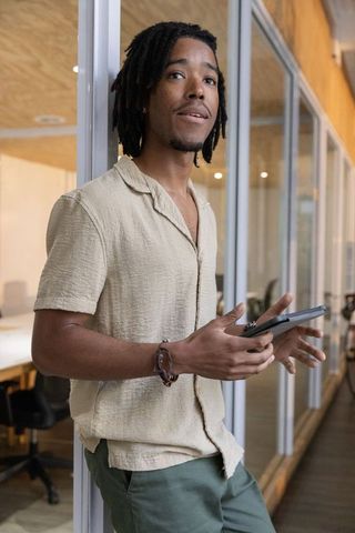 African american man leaning on glass wall holding tablet in modern workspace