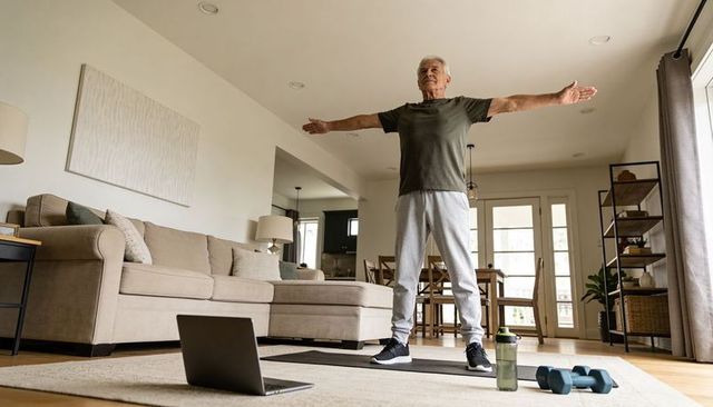 Senior man stretching at home with laptop and dumbbells for active aging workout