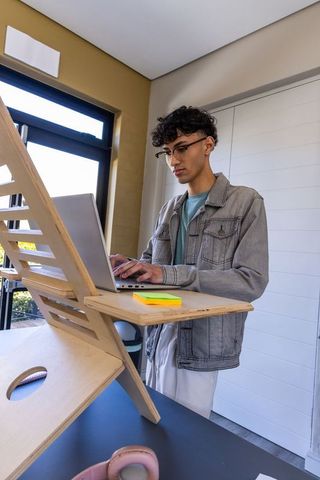 Young asian man standing at wooden riser working on laptop in bright home office
