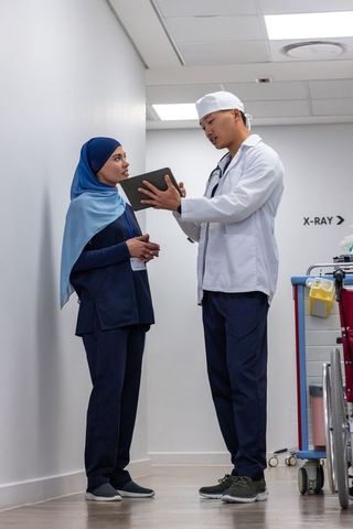 Doctor and nurse discussing tablet scan in hospital corridor near x-ray sign
