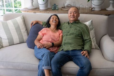 Senior asian couple sitting on sofa laughing together in cozy neutral living room