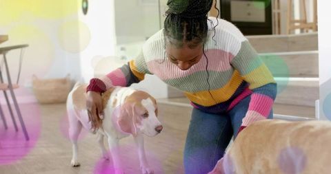 Kneeling woman petting two tan-and-white dogs at home wearing colorful striped sweater