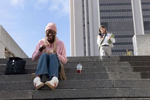 Diverse women sitting on urban steps eating lunch, checking phone, carrying notebooks