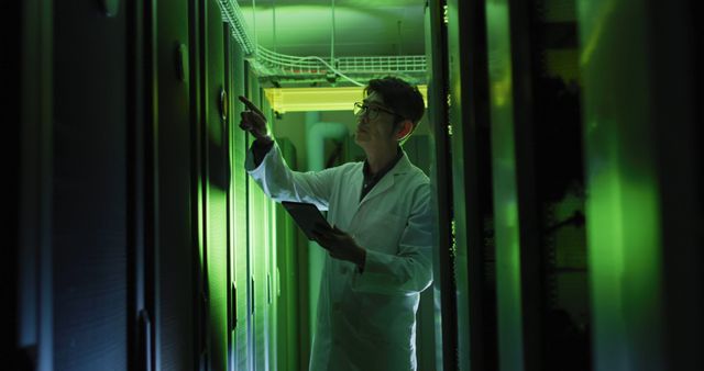 Scientist in lab coat operates equipment in data center illuminated by green lights. Useful for illustrating themes of technology, cybersecurity, data management, and tech workplace. Ideal for use in articles about data science, IT infrastructure, research advancements, and secure data storage solutions.