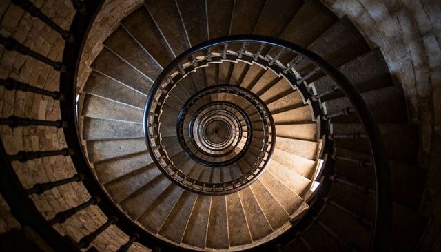 Spiraling masonry staircase descending through narrow tower with concentric metal railing
