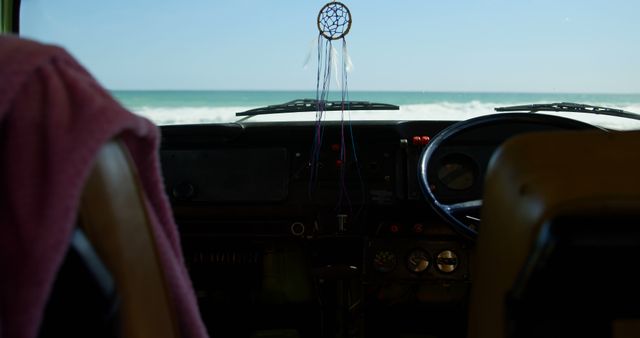 Car windshield framing a scenic ocean view with a dreamcatcher hanging from the rear-view mirror. Ideal for use in travel blogs, vacation promotions, or automotive advertisements showcasing relaxed and adventurous lifestyles.