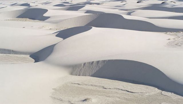 Sunlit white sand dunes rippling with dramatic shadows and wind-formed ridges in arid desert