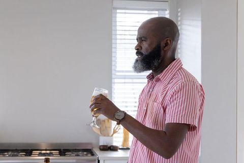 Elegant mature african american man holding glass in modern kitchen