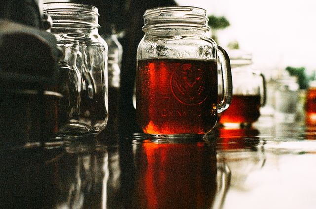 Rustic mason jars filled with iced tea on a reflective surface. The image is suitable for promoting summer beverages, homemade drink recipes, and rustic-themed decor. Perfect for use in advertising campaigns, social media posts, or website banners related to food and drink.