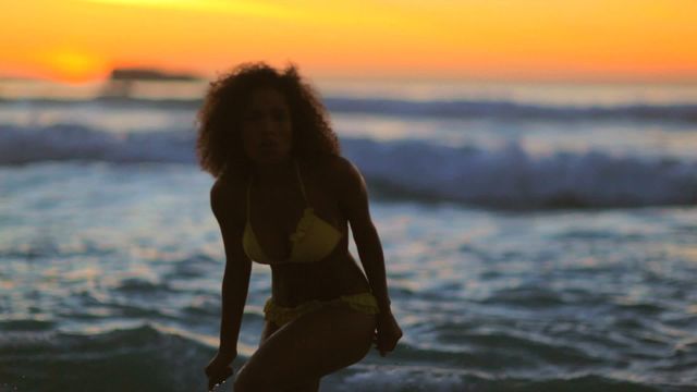 A cheerful woman is dancing in the ocean with a stunning sunset backdrop, creating a vibrant summer scene. This image captures the feeling of leisure and happiness, making it ideal for use in advertising beach resorts, travel magazines, summer promotions, or wellness articles focusing on joyful outdoor activities.