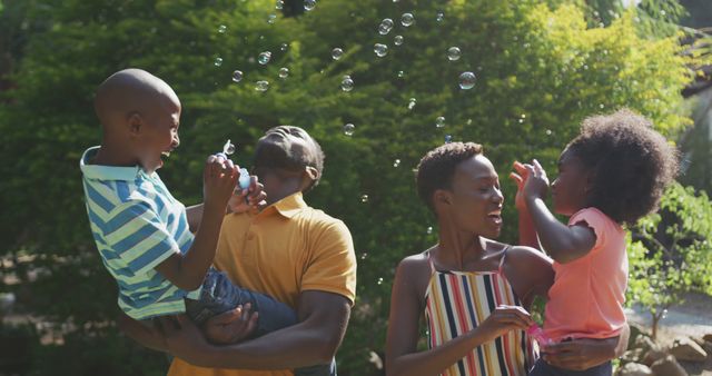Happy african american family embracing and blowing bubbles in garden. Lifestyle, domestic life, family, and togetherness.