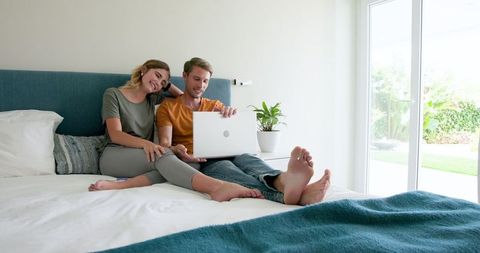 Couple enjoying leisure time with laptop on bed in bright room