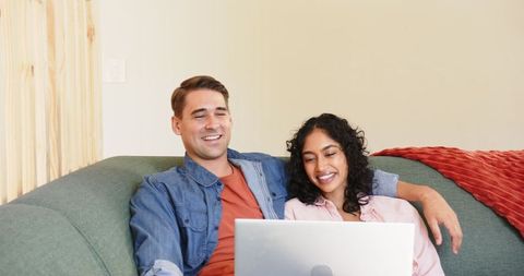 Diverse Couple Relaxing on Sofa Using Laptop at Home Together